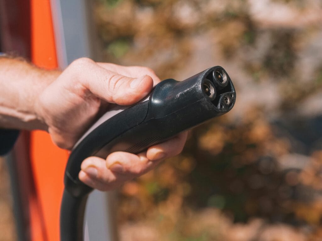 Hand Tesla charger plug, symbolizing clean energy and innovation.