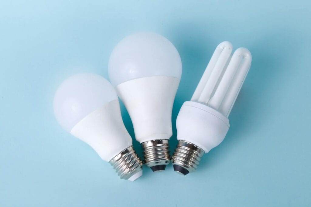 Three assorted LED and CFL light bulbs against a light blue background.